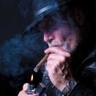 Man in Fedora Lighting Cigar Surrounded by Blue Smoke