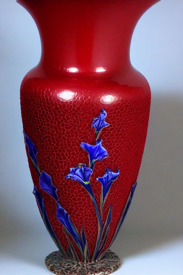 Red crackle-glaze vase with blue iris flowers and green stems on textured background