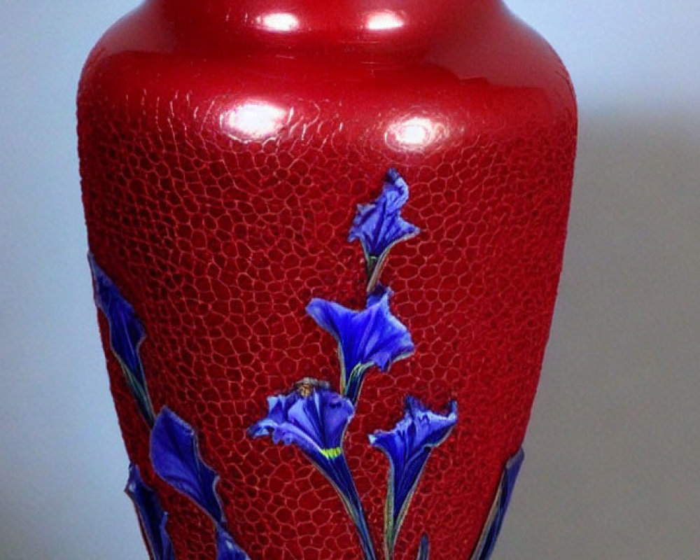 Red crackle-glaze vase with blue iris flowers and green stems on textured background