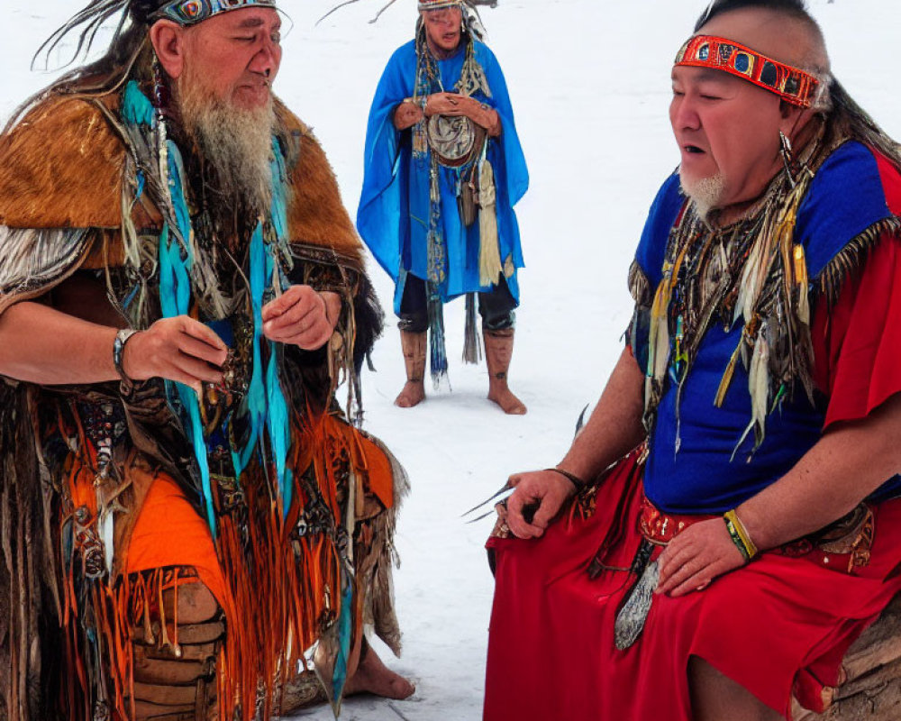 Three individuals in traditional Native American attire with feathered headdresses and beadwork conversing in snowy setting