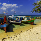 Wooden Boats on Sandy Beach with Clear Waters, Greenery, Mountains, Cloudy Sky