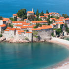 Picturesque island with rocky shores, red-roofed buildings, and church tower in clear blue sea