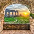 Ancient stone gateway frames Roman amphitheater arcades at sunset