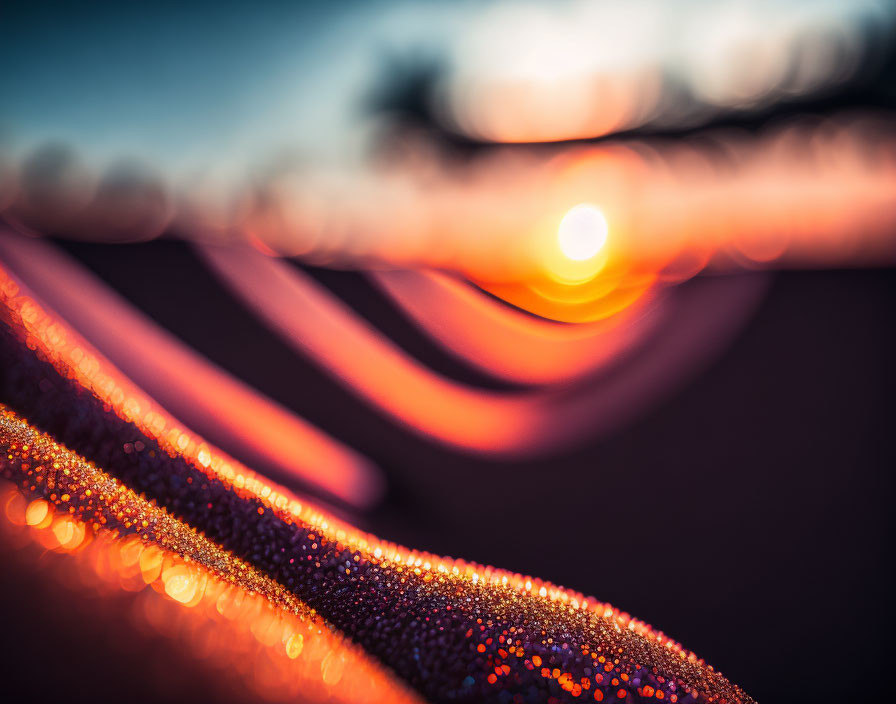 Macro photography of dew drops on surface with blurred sunset backdrop and warm color gradient.