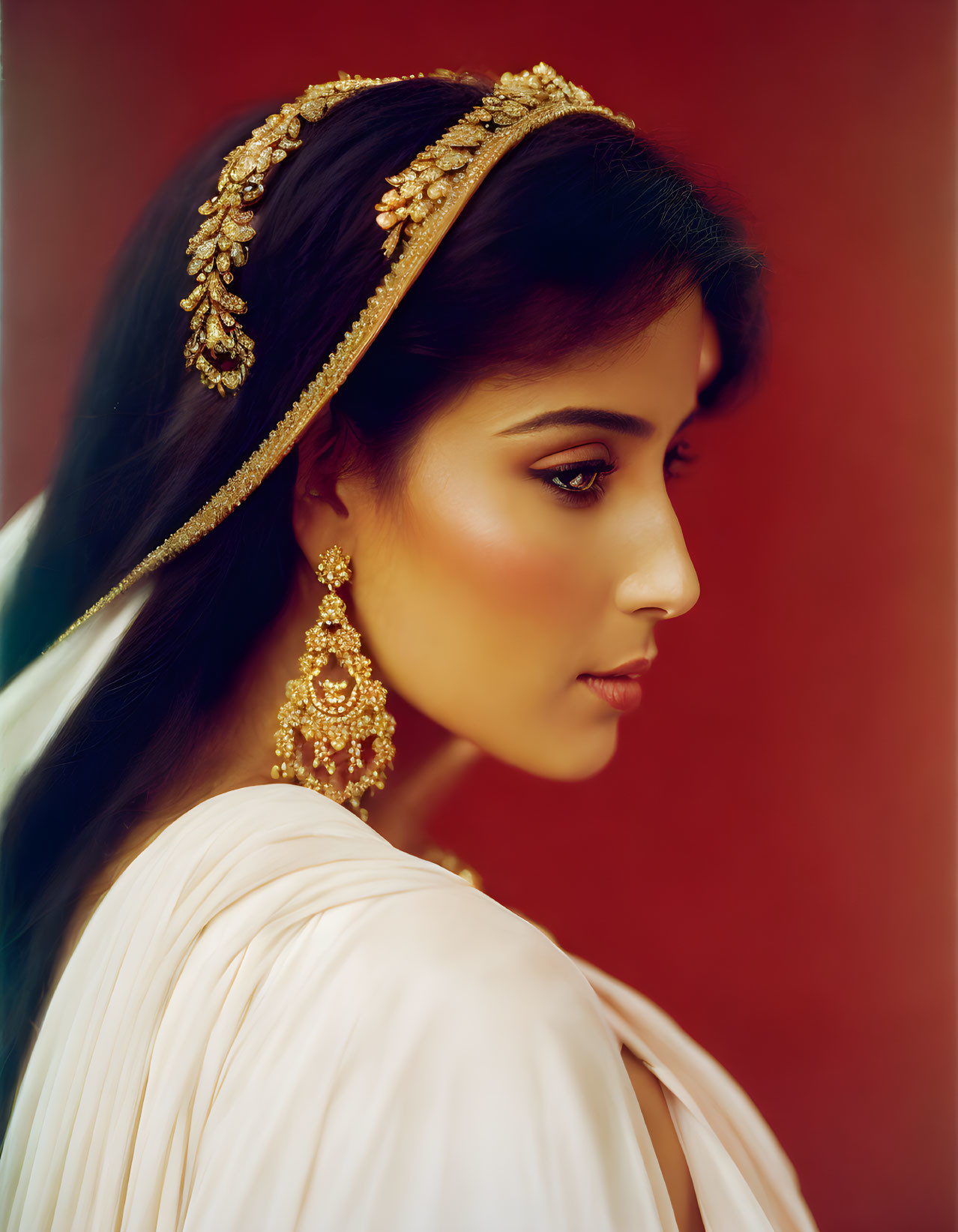 Profile of woman in gold jewelry and white attire on red backdrop