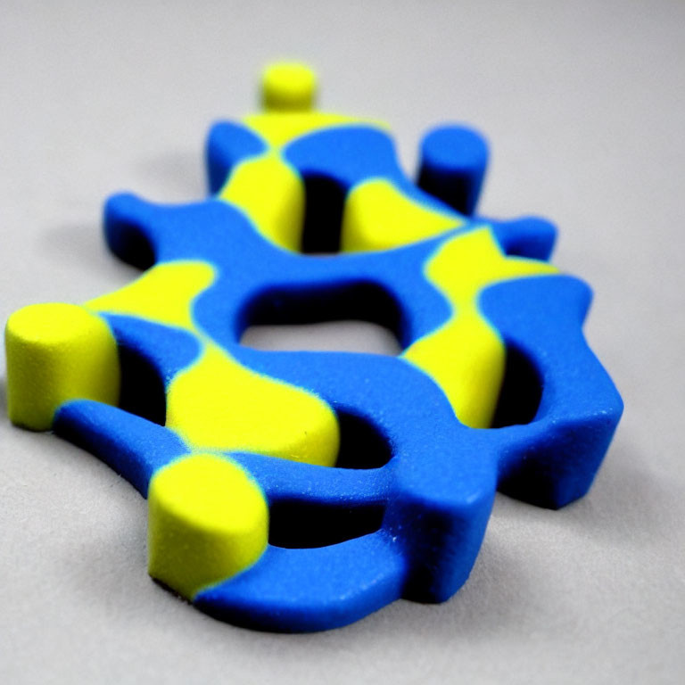 Blue and Yellow 3D-Printed Puzzle Piece on Grey Background