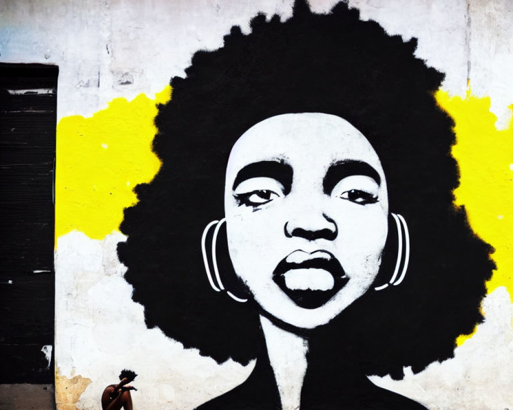 Monochrome mural of woman's face with afro and yellow splash, small figure nearby