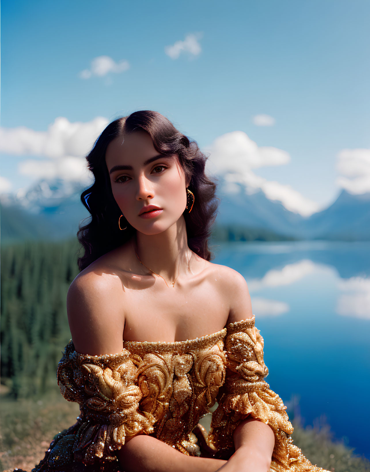 Dark-haired woman in golden off-the-shoulder dress by serene lake and mountains