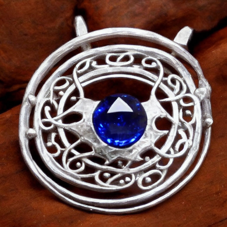 Circular Silver Pendant with Blue Gemstone on Wooden Background
