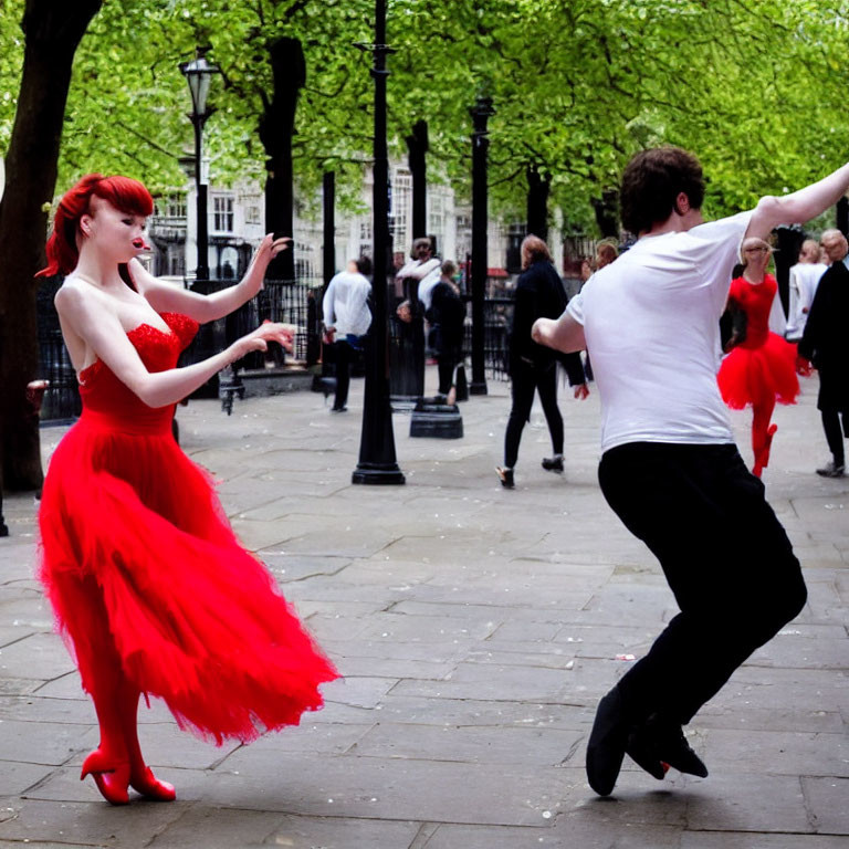 Outdoor couple dancing: woman in red dress, man in white shirt, others in background.