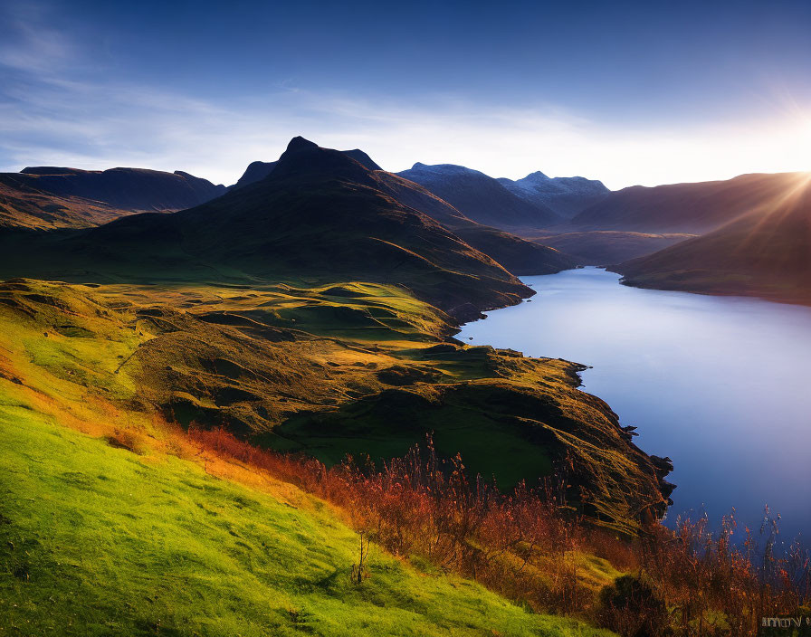 Tranquil lake at sunrise with lush green hills