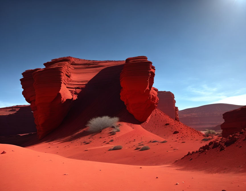 Vibrant red sand dune with stratified rock formations under clear blue sky