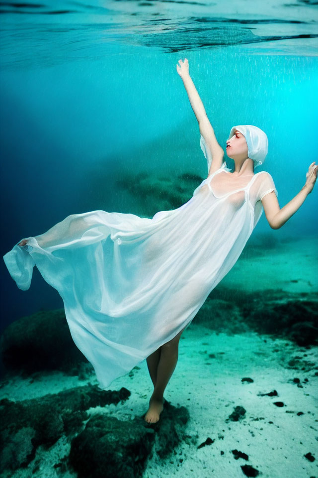 Underwater dancer in white dress and swim cap with flowing fabric under light.