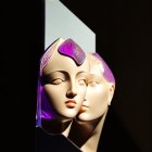 Glossy mannequin heads with purple accents on mirror against dark background