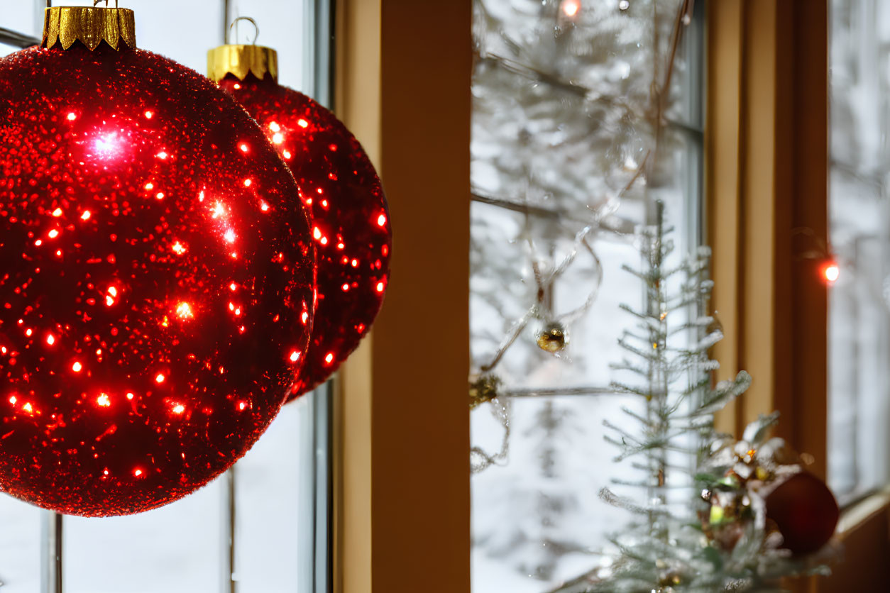 Vibrant red Christmas baubles by window with snowy landscape