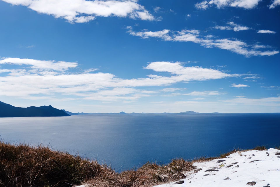 Blue Sea and Snowy Coastal Hill with Distant Mountains