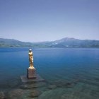 Golden Figure Statue in Blue Water with Mountain Backdrop at Sunset