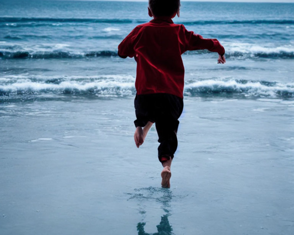 Child in red shirt running towards sea on beach horizon