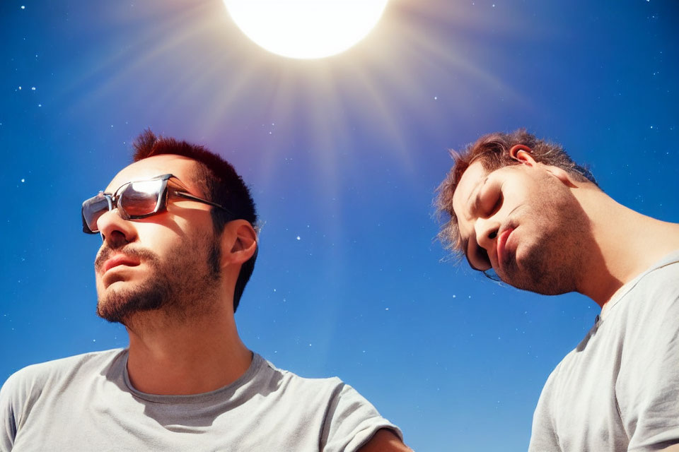 Two men with closed eyes in sunlight, one with sunglasses, under blue sky