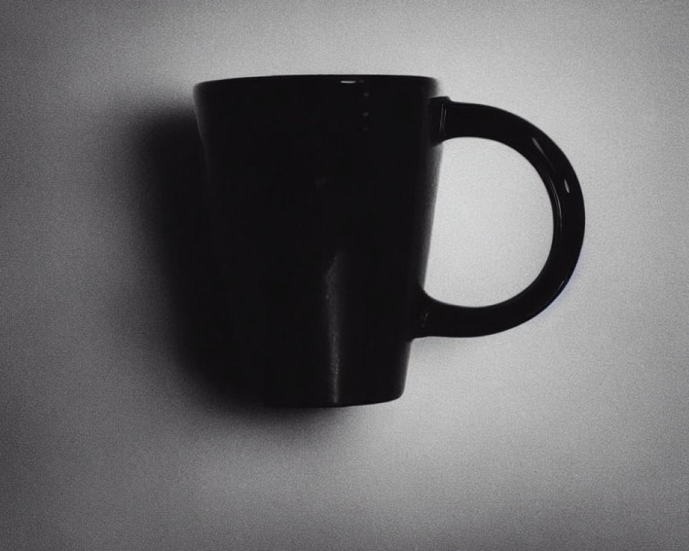 Black Coffee Mug Silhouetted Against Light Gray Wall