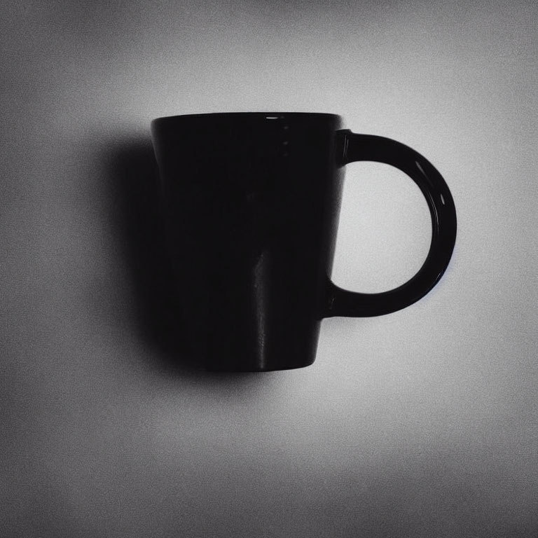 Black Coffee Mug Silhouetted Against Light Gray Wall