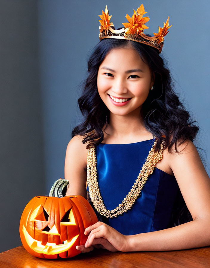 Smiling woman in blue dress with leaf crown holding carved pumpkin