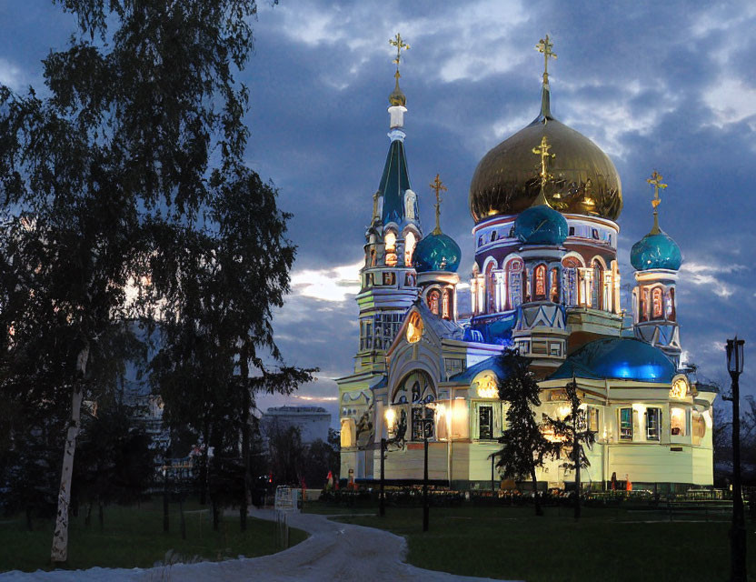 Orthodox cathedral with golden domes in evening light, set in lush scenery.