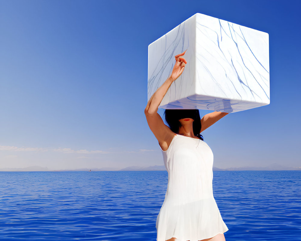 Person balancing large white cube with blue marble patterns by calm sea