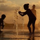 Children playing with water at sunset: one standing, one sitting.