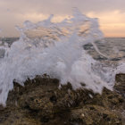 Majestic wave crashing on rocky shores at sunset