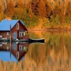 Colorful painting of red barn and lush trees reflected in serene water