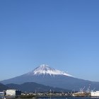 Mount Fuji overlooking serene town with buildings and greenery under clear sky