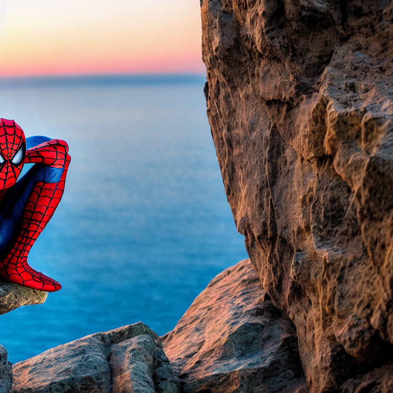 Person in Spider-Man Costume on Rocky Cliff with Ocean Sunset