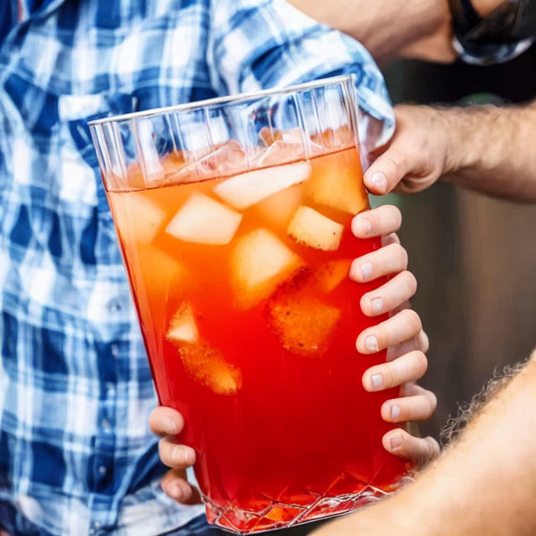 Close-up: Hands holding large glass pitcher with iced red punch