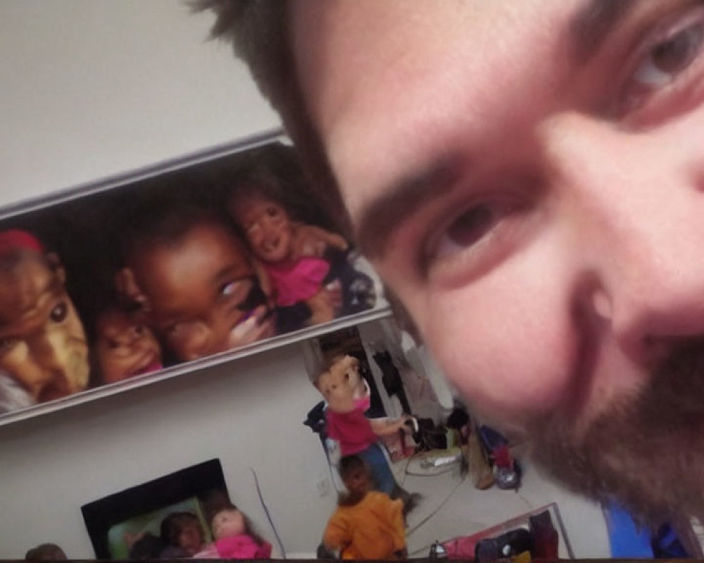 Man taking selfie with blurred background of children's toys and framed photo