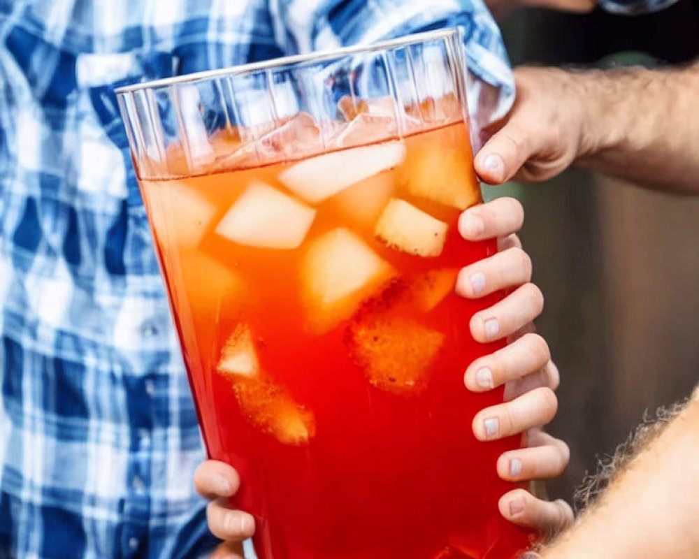 Close-up: Hands holding large glass pitcher with iced red punch