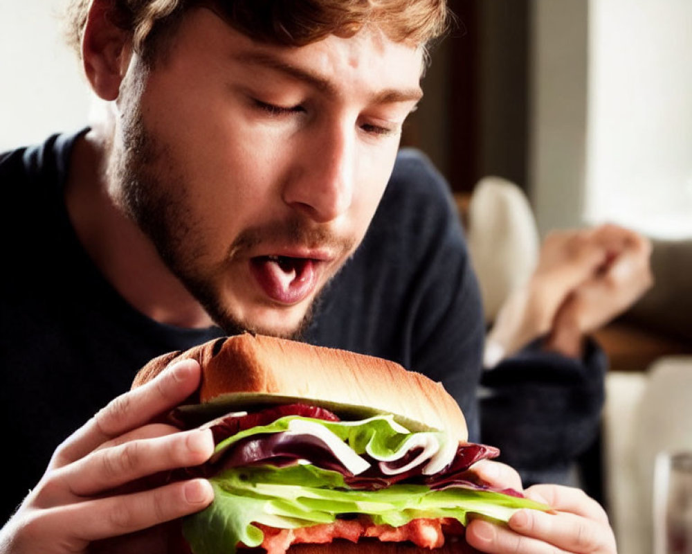 Bearded man eating a sandwich with lettuce, tomato, and meat