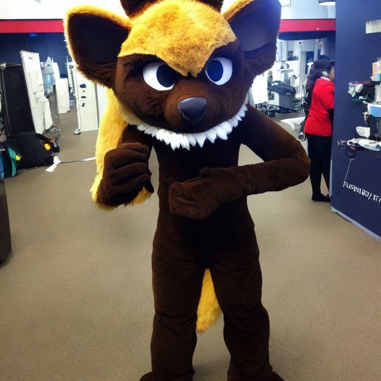 Brown Mascot Costume of Animated Fox with Big Eyes and Sharp Teeth Standing Indoors