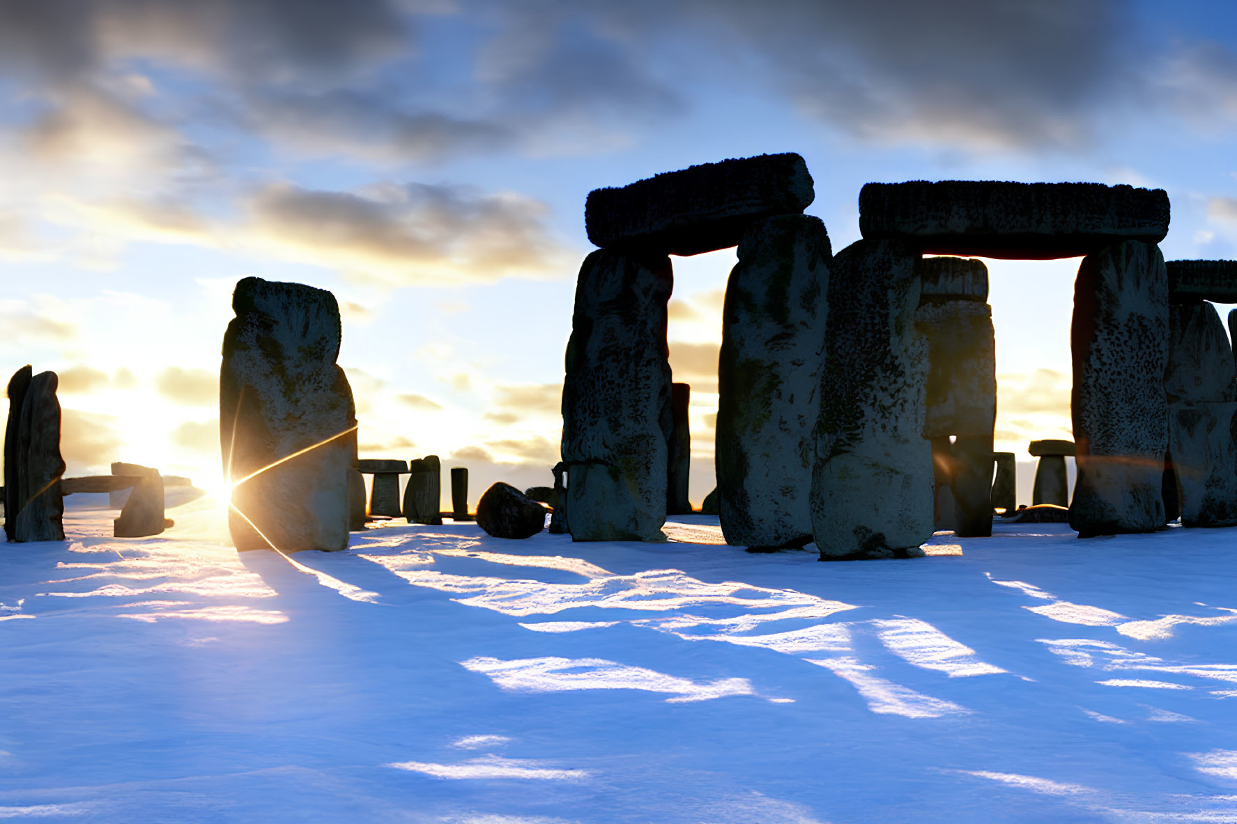 Snow-covered Stonehenge at sunrise under clear blue sky