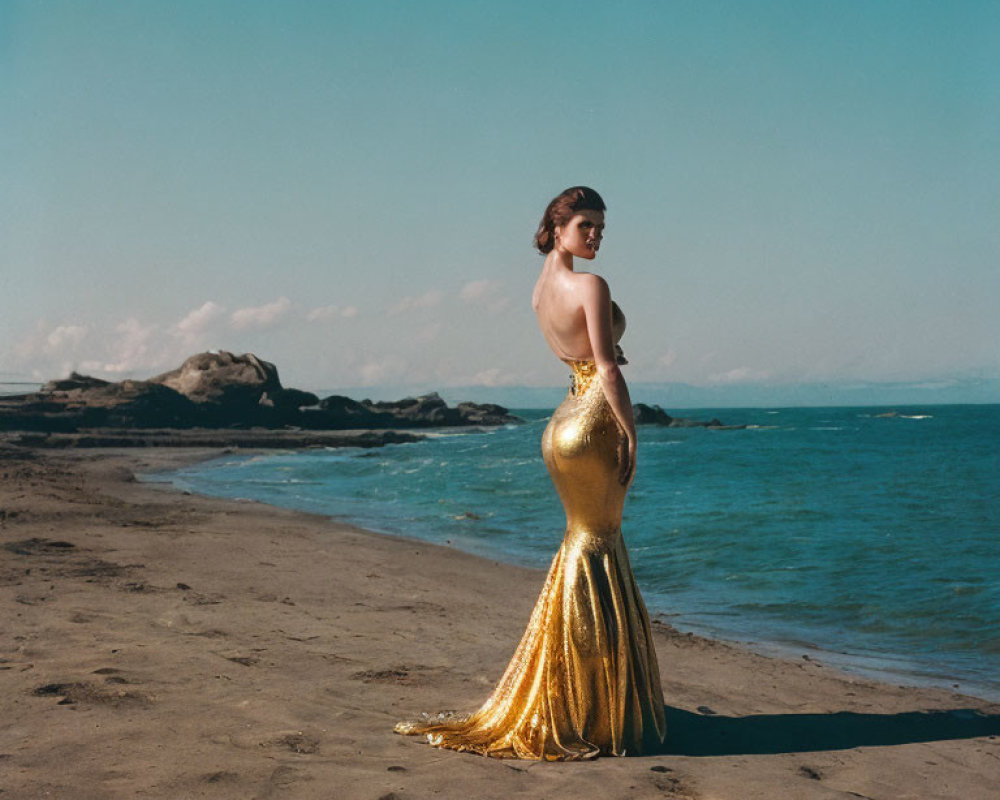Woman in gold mermaid gown gazes at rugged beachscape