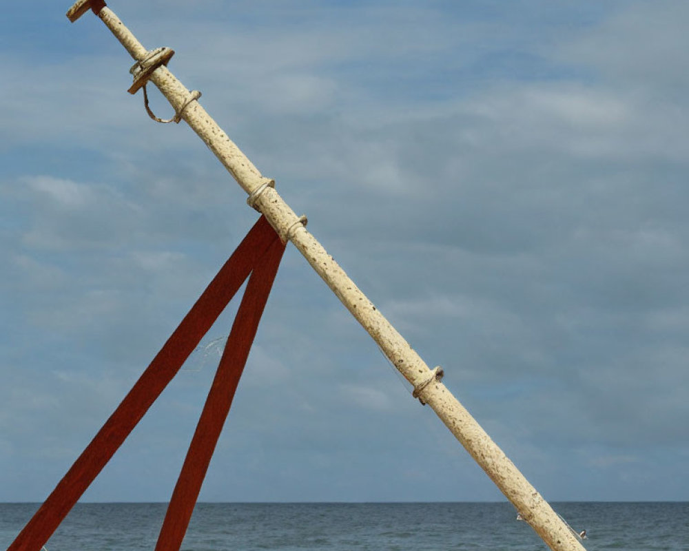 Weathered wooden swing set with rusty metal poles on sandy beach under cloudy blue sky