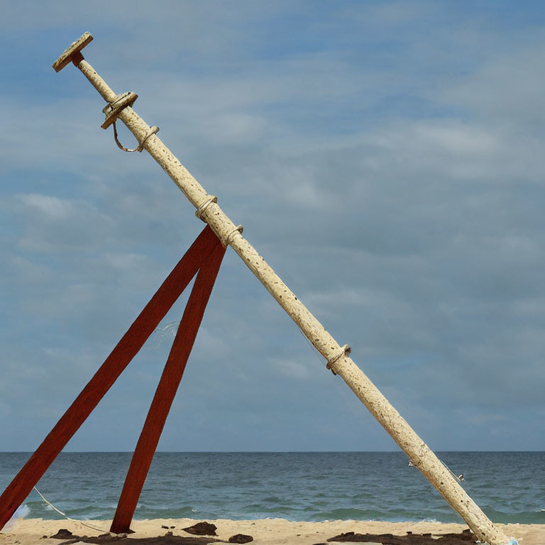 Weathered wooden swing set with rusty metal poles on sandy beach under cloudy blue sky