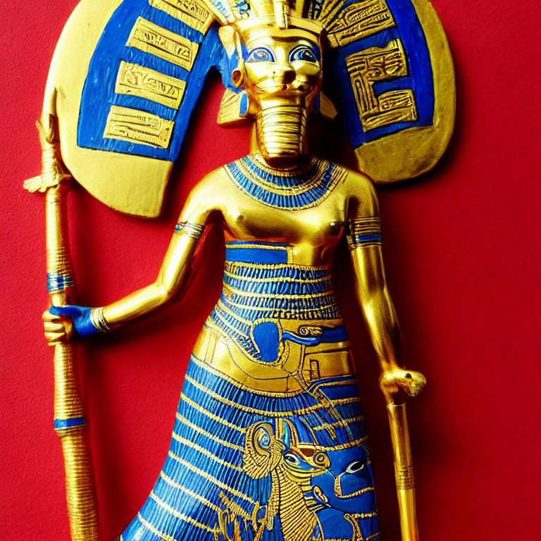 Golden and blue ancient Egyptian deity figurine with staff on red background