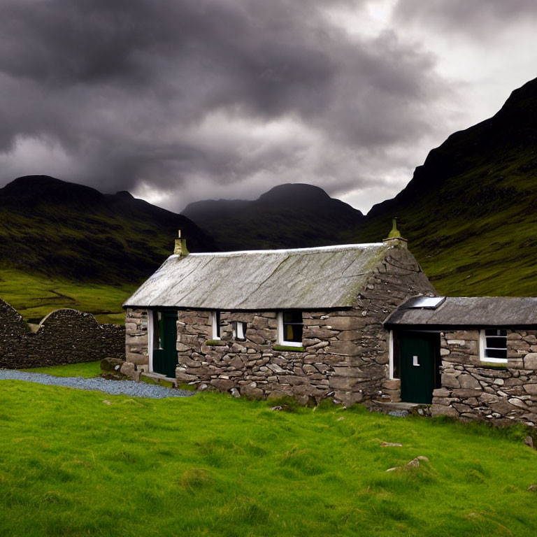 Stone cottage with slate roof in lush valley under dramatic sky.