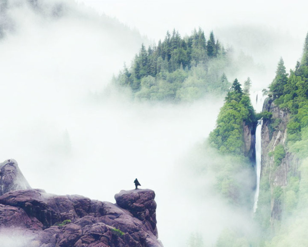 Person sitting on rocky outcrop overlooking misty forest with waterfall.