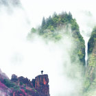 Person sitting on rocky outcrop overlooking misty forest with waterfall.