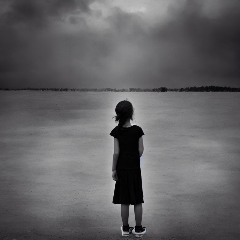 Lonely young girl in black dress in desolate landscape under cloudy sky
