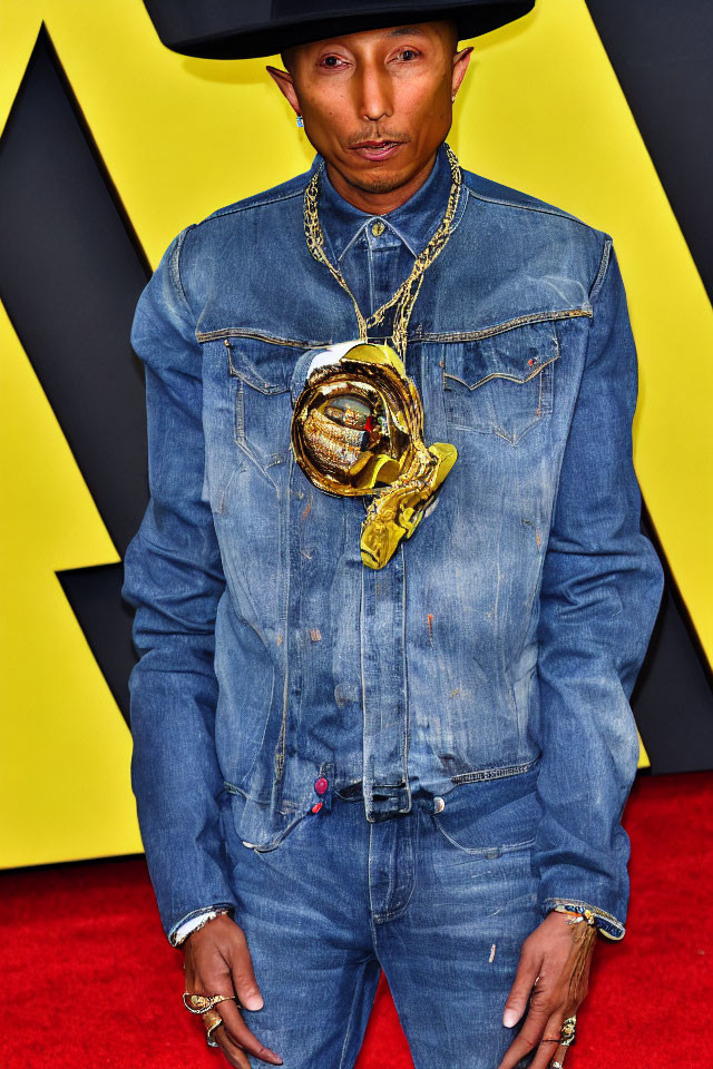 Person in denim outfit with necklace and hat against yellow and black background