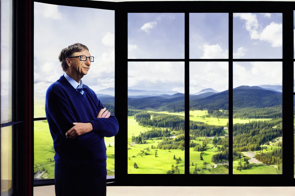 Person standing indoors by large window with scenic view of green hills and forests