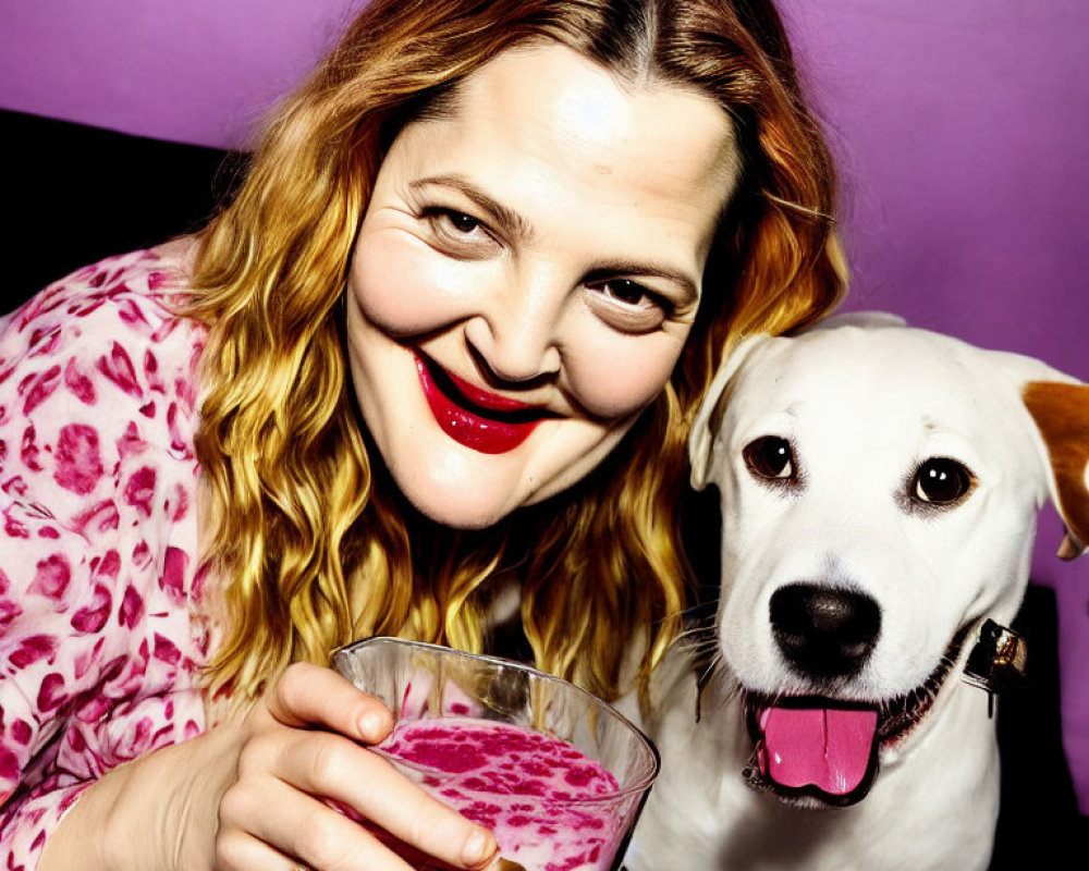 Smiling woman with red lipstick and wavy hair holding pink drink next to happy white dog